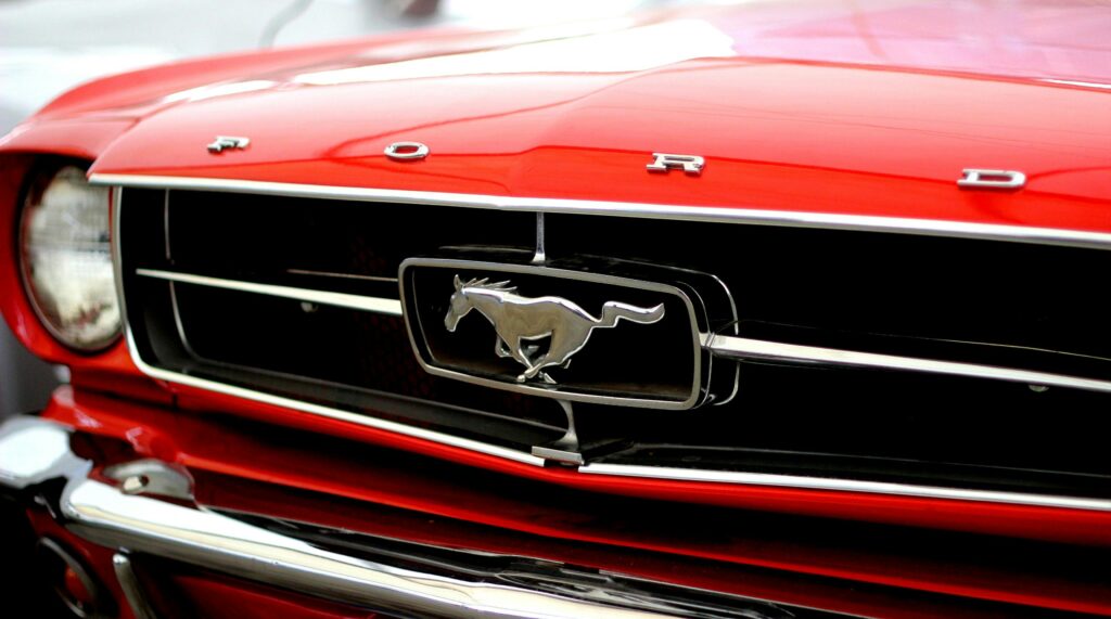 Close-up image of a vintage red Ford Mustang's iconic front grille and logo.