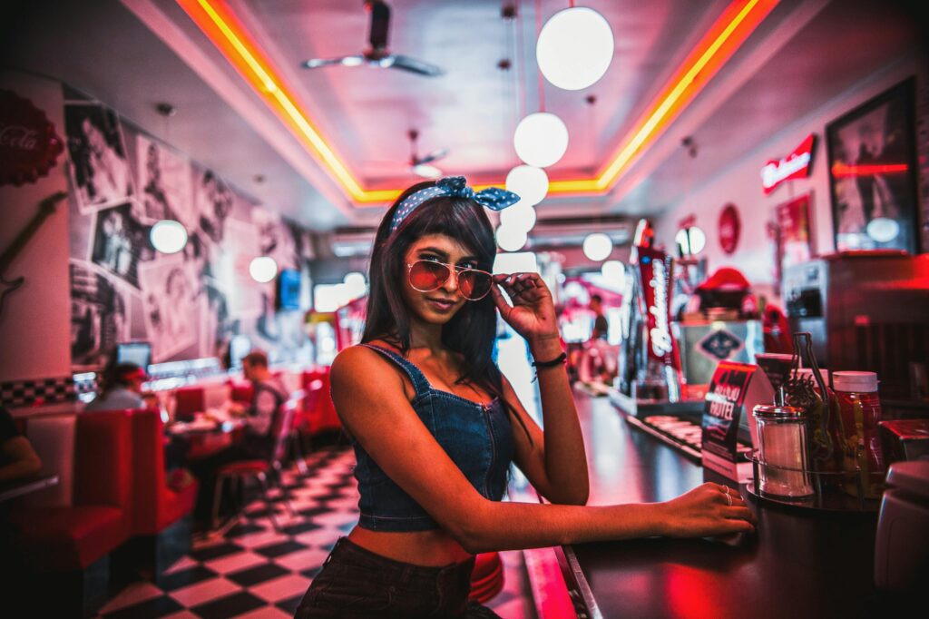 A fashionable woman poses at a retro diner counter, exuding glamour and style.