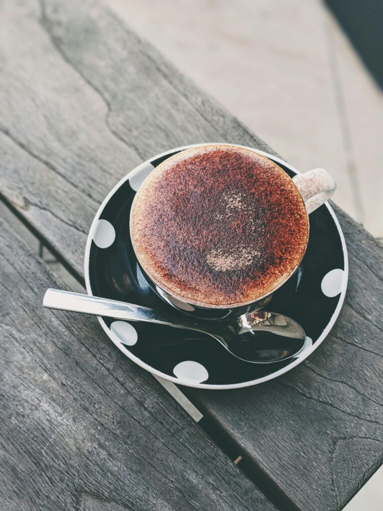 A cozy cappuccino in a polka dot cup with saucer and spoon on a rustic wooden table.