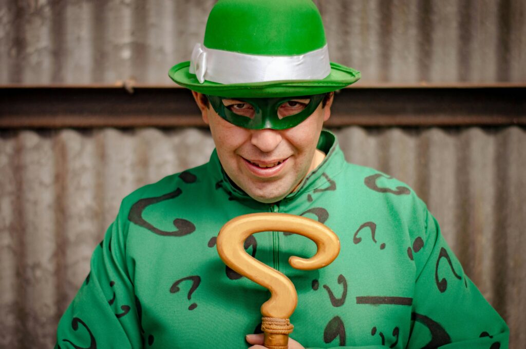 A mysterious man in a green costume with question marks, holding a cane and wearing a hat and mask.