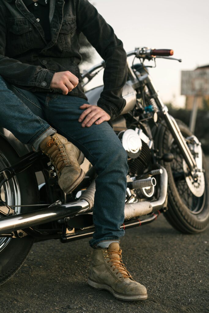 Man sitting on a motorcycle wearing jeans and boots, enjoying a relaxed moment outdoors.