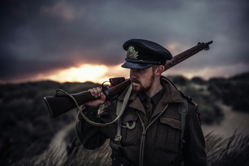 A soldier in uniform holding a rifle against a dramatic sunset background.