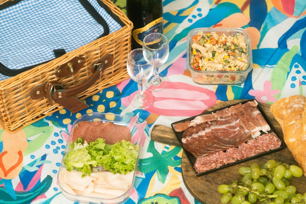 Colorful picnic arrangement featuring charcuterie, grapes, pasta salad, and a wicker basket.