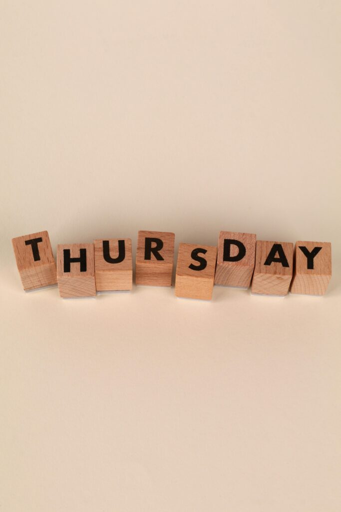 Wooden blocks spelling 'Thursday' on a beige background, minimal style.