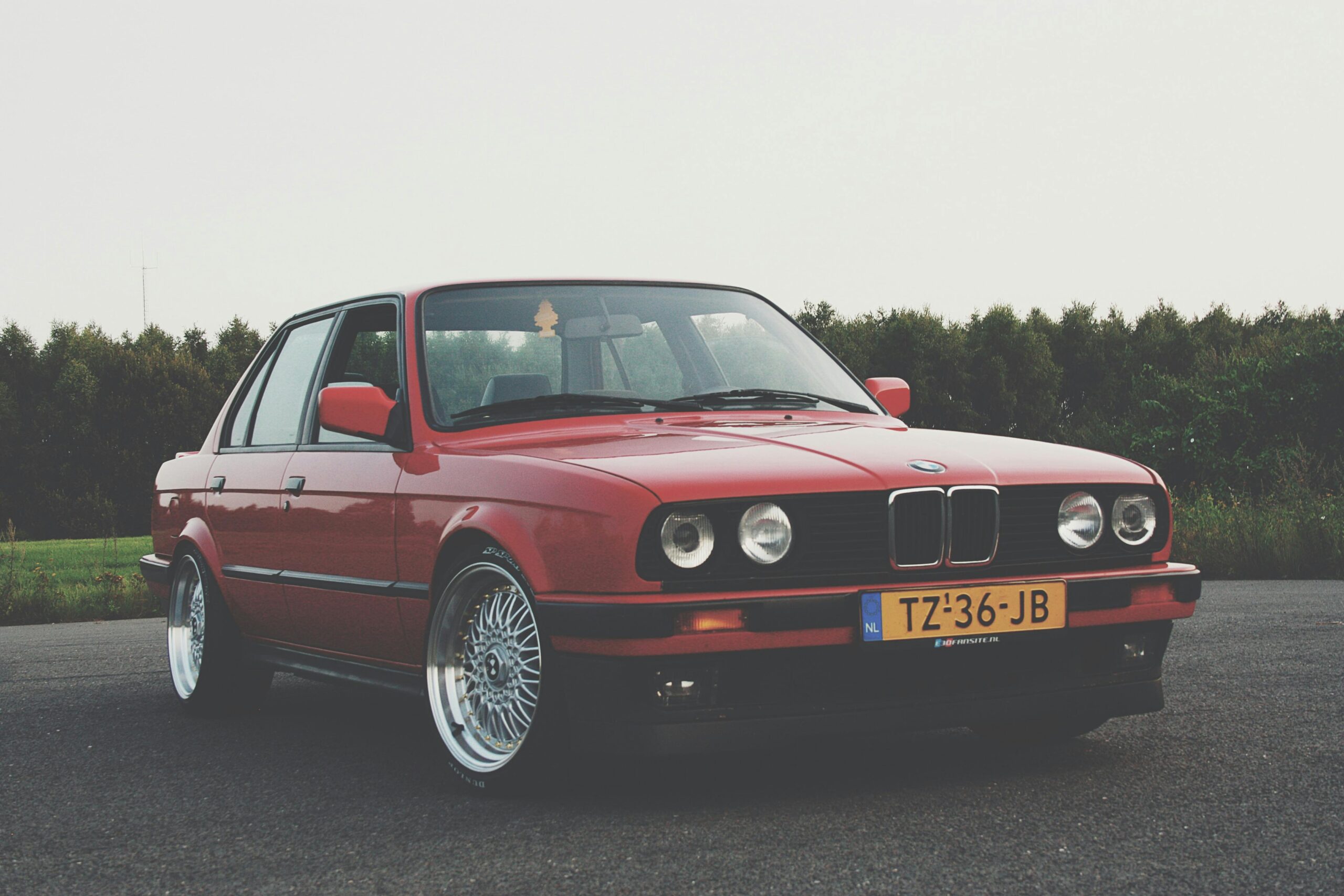 A classic red BMW E30 parked on an empty road, showcasing vintage automotive style.