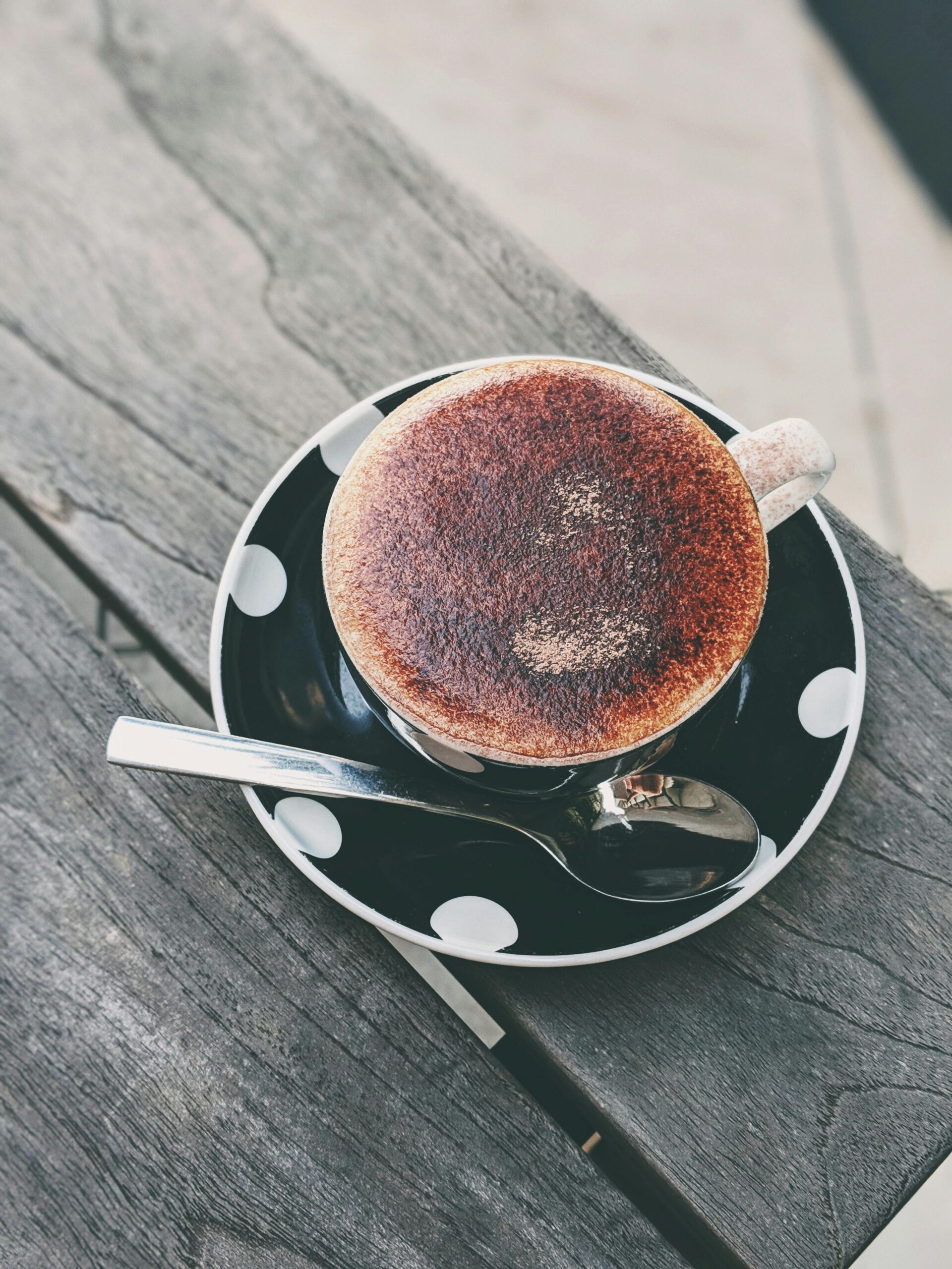 A cozy cappuccino in a polka dot cup with saucer and spoon on a rustic wooden table.