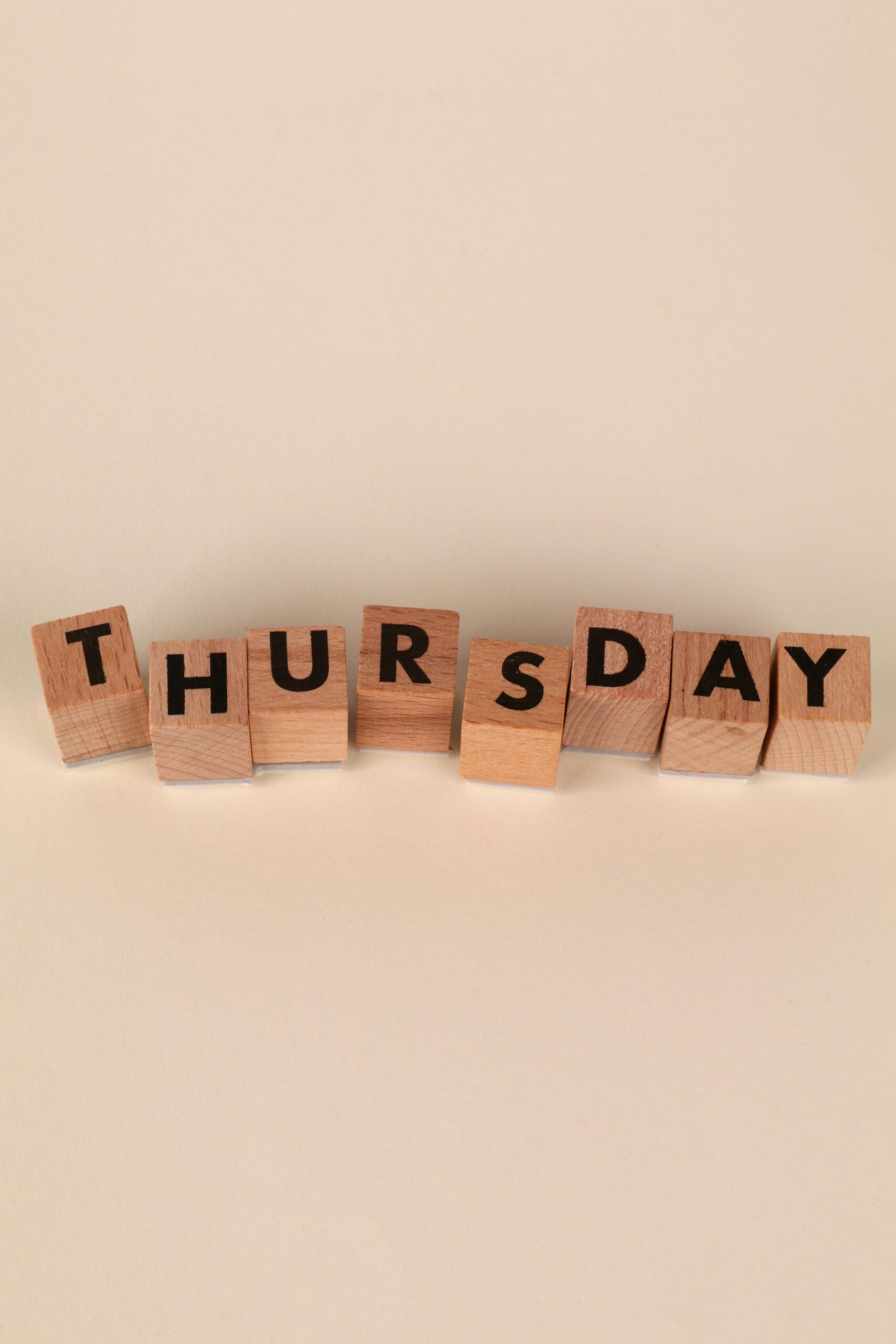 Wooden blocks spelling 'Thursday' on a beige background, minimal style.